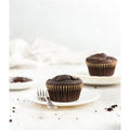Muffin's on a small plate with a fork resting on the plate with crumbs in the foreground and some icing and another muffin in the background