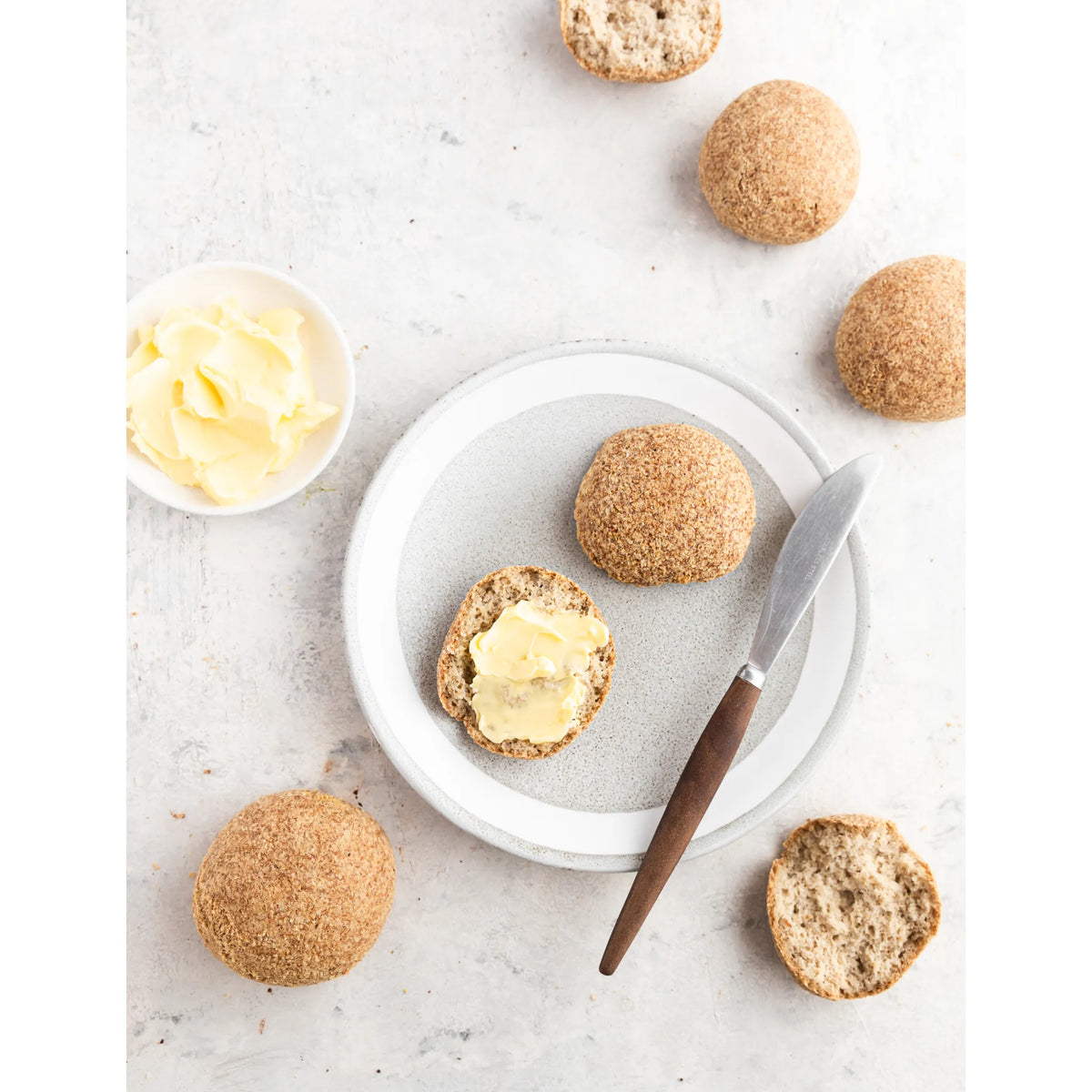 Buns on a plate with a knife and butter on a light surface