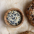 a small wooden bowl with Bagel Seasoning with a bagel on the right