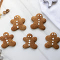Five gingerbread cookies shaped like men on a white surface with cookie cutters.