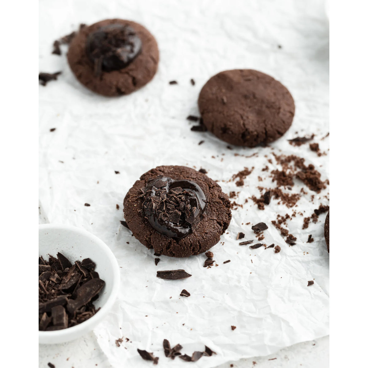 Chocolate cookies with a bowl of chocolate pieces on a white surface