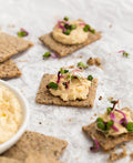 Crackers with hummus and garnishes on a light surface