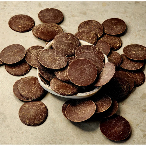 Solomon's Gold Dark Chocolate Buttons 70% spilling out of a small bowl on a beige background
