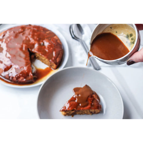 Sticky Date Pudding with a slice on a plate with sauce being poured onto it.