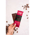 Hand holding a Solomons Gold chocolate bar and packaging with scattered cocoa beans on a light background