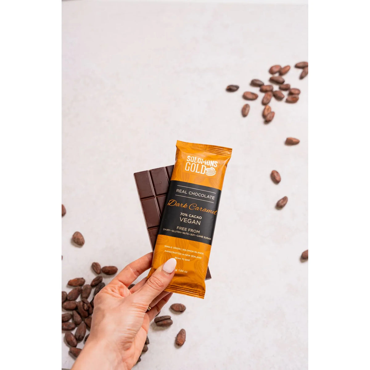 Hand holding a Solomon's Gold vegan chocolate bar with cacao beans on a light background