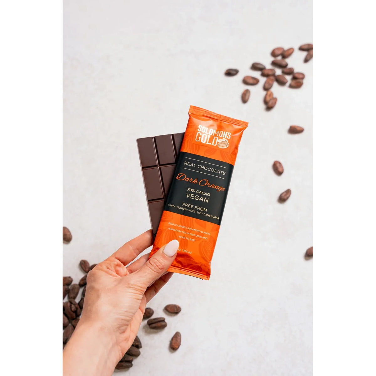 Hand holding a chocolate bar package with cacao beans on a light background