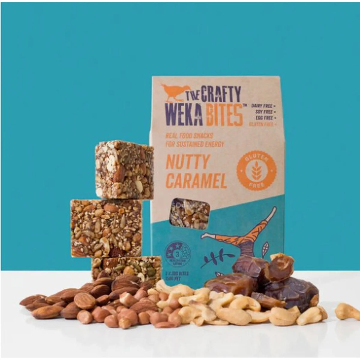 The Crafty Weka Bites Nutty Caramel snack bars with packaging on a white surface against a blue background