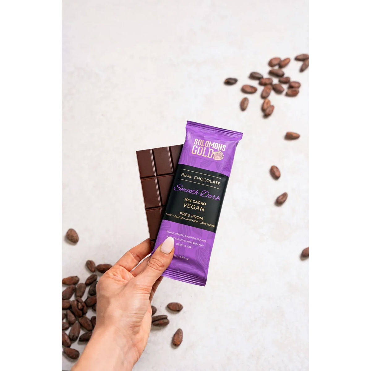 Hand holding a Solomons Gold chocolate bar and packaging with cacao beans on a light background